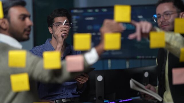 A young engineer with a pen at his chin thinks for a beat and then points at the note that answers his colleague's question inside a dimly lit machine learning startup office.