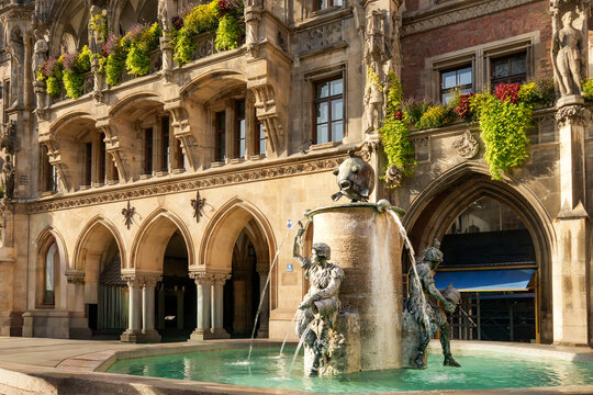 Close-up of the famous Fish Fountain in Munich with bronze sculptures pouring water. Neo-Gothic New Town Hall (Neues Rathaus) facade in the background on a sunny day.