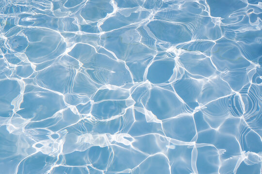 Clear blue swimming pool water surface texture background with sunlight reflection