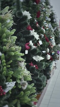 Row artificial decorated Christmas trees in mall store shop. New Year Eve. Holiday. Retail store display. Preparation winter season celebration. Festive decor selection shopping. Vertical shot