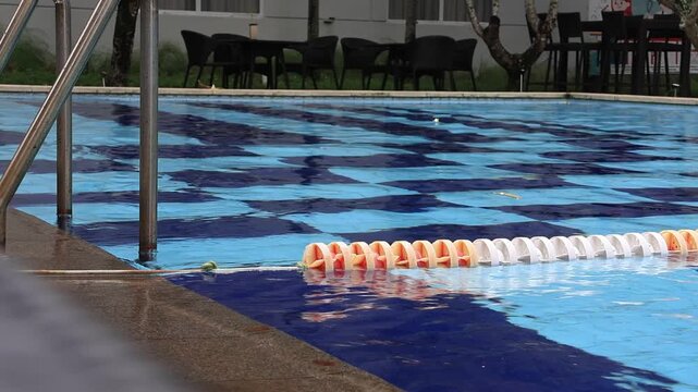 Swimming pool lane divider floats on water surface. Orange and white plastic floats form a line. Blue water ripples gently around the divider. Ideal for fitness, sports, or aquatic activity scenes