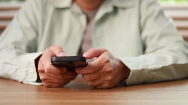 Close-up view of male hands typing text on smartphone touch screen at wooden desk. Modern digital communication, mobile messaging, online business, and social network connection concept