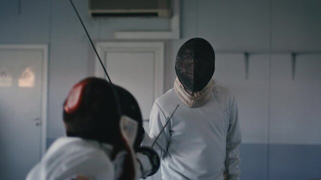 Fencing sport. Sportsmen fencing training. Two swordsmen are doing sword moves. Fencer players in gym, indoor sports club. Two athletes practice epee, uniforms and masks. Olympic combat sport.