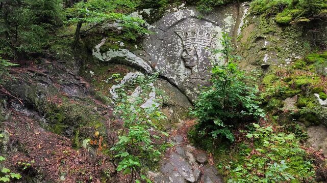 Historical rock relief carving of Stephen the Great crowned profile embedded in a mossy stone wall in a Gura Humorului forest.