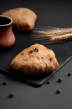 Freshly baked triangular samsa pie with black sesame seeds on slate board. Traditional savory pastry on dark wooden background.