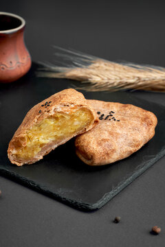 Sliced savory samsa pie with potato filling on black slate board. Traditional baked pastry with sesame seeds on dark background.
