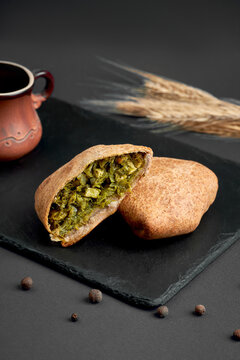 Halved baked samsa pie filled with savory spinach and herbs on black slate board. Delicious vegetarian pastry on dark background.