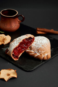 Halved sweet baked pie with juicy cherry filling dusted with powdered sugar on slate board. Dessert pastry on dark background.