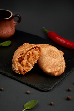 Halved savory baked pie with braised cabbage filling on slate board. Traditional homemade pastry on dark background with chili pepper.