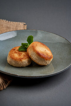 Golden cottage cheese pancakes garnished with fresh mint on ceramic plate. Traditional syrniki breakfast served on dark background