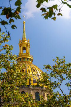 Golden dome of les invalides framed by green tree leaves in paris
