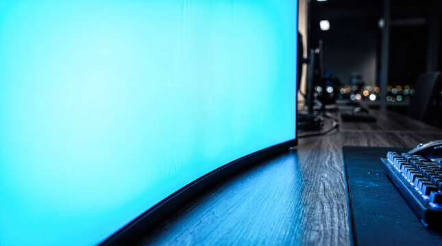 Glowing blue blank computer monitor screen resting upon dark wooden desk beside mechanical keyboard during late night hours inside modern office