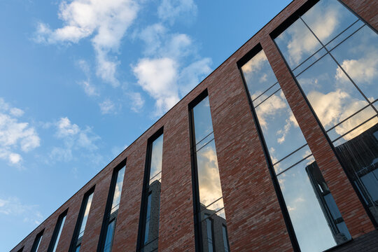 Modern brick building with large glass windows and balcony against blue sky with clouds
