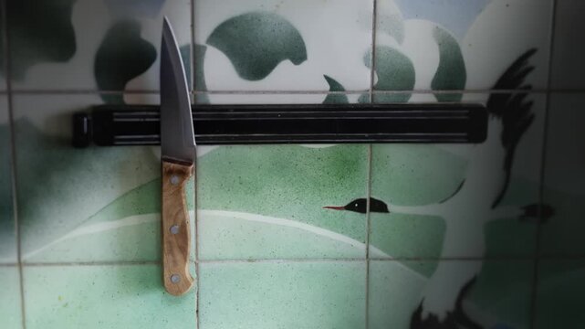 Male hand removes and then attaches variety of knives to magnetic holder in kitchen, tiled wall.