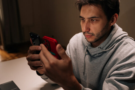 Portrait of man holding and comparing two smartphones simultaneously, concentrating on multitasking work, managing multiple digital devices and personal technology, staying connected in modern life.
