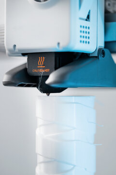3D printer head printing a detailed white plastic component