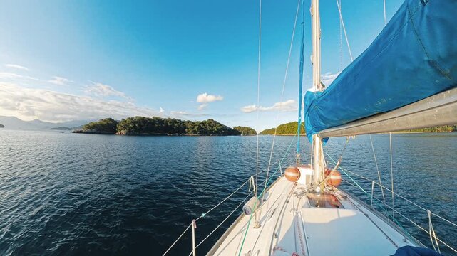 View from the deck of a sailboat across calm coastal water toward forested islands on a sunny day