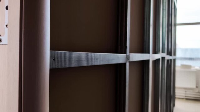 Metal stud framing installation for interior partition wall construction, showing structural support elements with wooden panel detail on left and bright window light in background