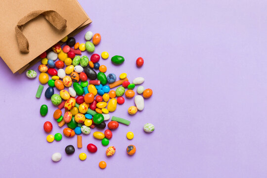 shopping paper gift bag in corner full of assorted traditional candies falling out on colored background with copy space. Happy Holidays sale concept