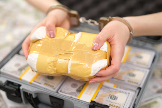 Close view shows restrained hands gripping taped parcel over open suitcase packed with bundled cash, creating strong visual links to arrest, bribery, smuggling, seized evidence, corruption, and