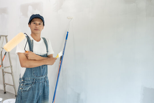 Portrait painter man show brush for products to restore and paint the wall, indoor the building site of a house, wall during painting, renovation, painting, contractor, Architect, construction worker