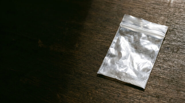 Small transparent plastic ziplock bag with white powder residue lying on dark wooden table