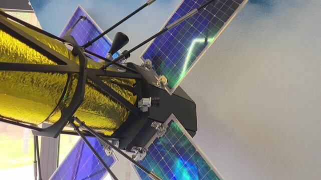 Close up view sophisticated satellite model featuring golden thermal insulation and large blue-hued solar panels, part of an educational space exhibit indoors