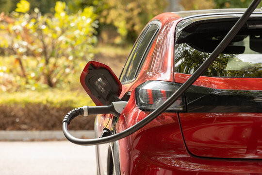 Red Electric Car Connected to Charging Cable in Sunny Outdoor Setting, Representing Electric Mobility, Sustainable Transportation and Clean Energy