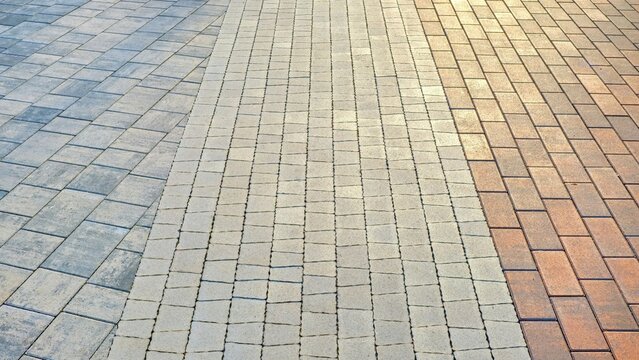 Multi-colored concrete paving stones perspective background. Three different patterns and shapes of stone tile blocks on pedestrian walkway.