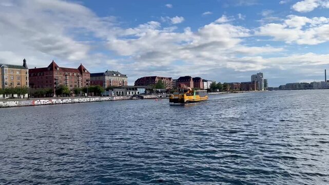 Yellow public transport boat, also known as a Harbour Bus, navigating the waters of Islands Brygge in Copenhagen, Denmark, passing by the city's waterfront with its distinct architecture - stock video