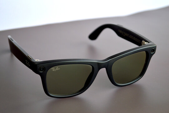 Modern Ray-Ban smart glasses with built-in cameras displayed on gray surface, showcasing innovative wearable technology and stylish black wayfarer design