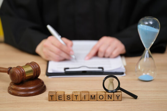 In a court setting, a judge prepares to take notes while an hourglass measures time. Blocks spell out TESTIMONY, capturing the essence of the legal moment.