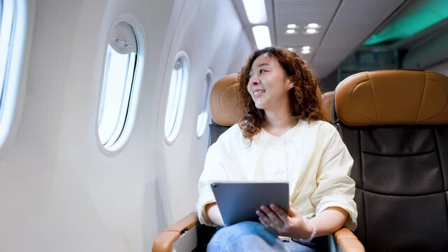 Smiling passenger using a tablet in an airplane window seat, lit by cabin lights during flight, conveying leisure travel, inflight entertainment, and a modern connected lifestyle.
