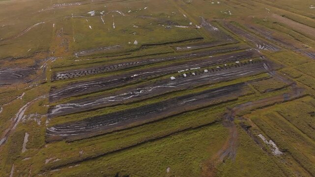 An aerial drone shot reveals a working peat bog in rural Ireland, featuring stacks of drying turf and bagged fuel ready for transport. Authentic rural industry and landscape.