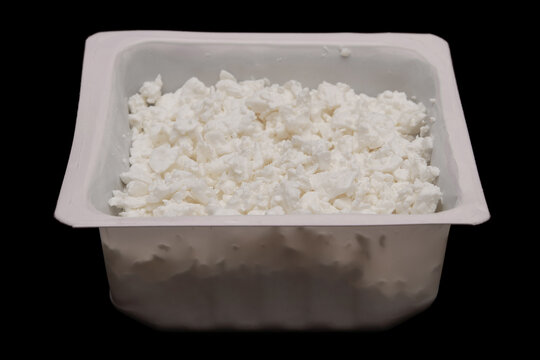 Cottage cheese in container isolated on black background. Side view. Pressed milk solids