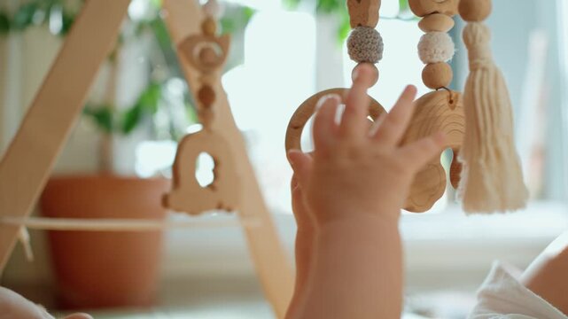 Adorable little baby's hands reaching for and playing with natural wooden toys hanging on a baby gym. Infant boy exploring different textures and shapes. Promoting sensory and motor skill development