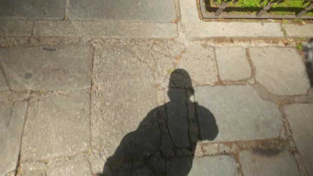 A topdown view showing the shadow of a person walking along a stone path in Madrid, Spain. Captures an authentic urban travel moment during golden hour.
