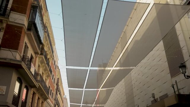 Low angle view of modern sun shade sails installed between historic buildings in Madrid, Spain. Ideal for travel, urban planning, and summer heat mitigation themes.