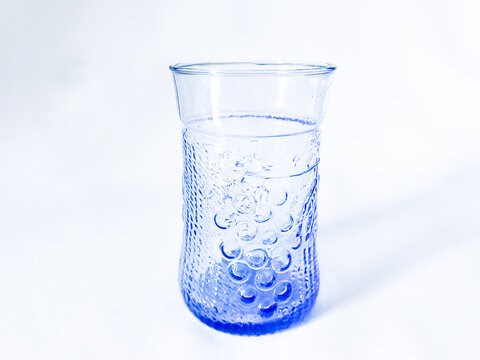 An empty light blue embossed glass tumbler with grape pattern texture, isolated on a white background.