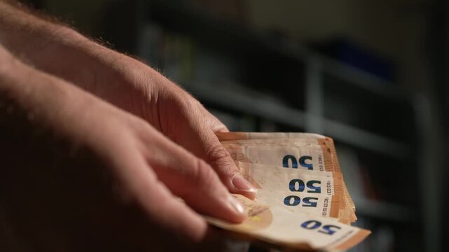 Close up of a mans hands counting a stack of 50 euro notes in low light. Suitable for financial, startup, and economic crime concepts.