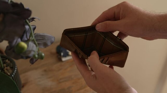 A man opens his leather wallet to find no money inside, illustrating financial struggle, poverty, or debt. Useful for banking, personal finance, and economic crisis concepts.