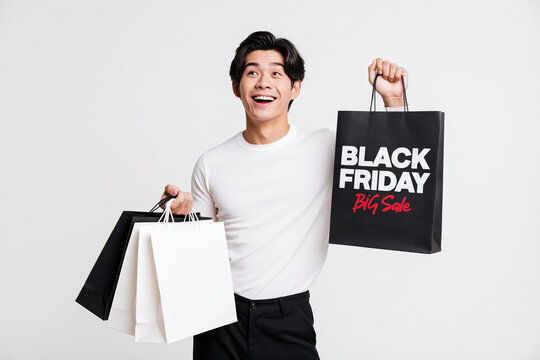 Excited Asian man in casual clothing holds shopping bags on Black Friday, expressing joy and anticipation for big sales.
