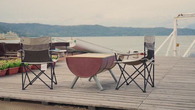 Relaxing outdoor setup with folding camping chairs and a barrel table on a wooden pier, offering a tranquil scenic view of Lake Toya in Hokkaido, Japan, perfect for a peaceful getaway and local food