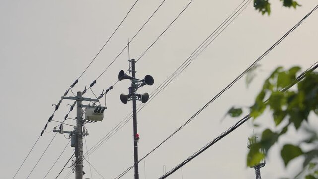 Utility pole with a public address system and a transformer against a cloudy sky in rural Hokkaido, Japan. Emergency alarm and alert technology for natural disasters or general announcements