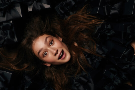A young woman with long, flowing brown hair and wide, expressive eyes is captured from above, amidst a dark.