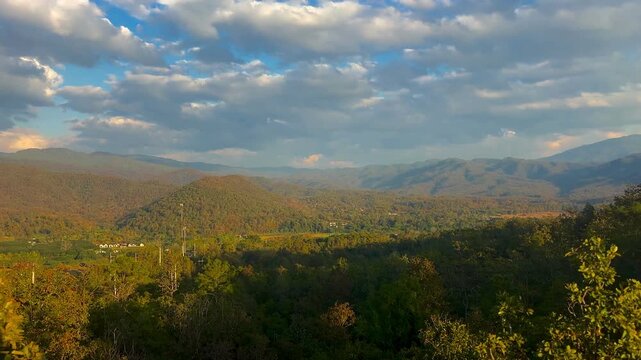 Wide mountain landscape over the Mae Hi valley in Pai Thailand with warm sunset light across forest covered hills and distant ridges beneath a dramatic cloudy sky
