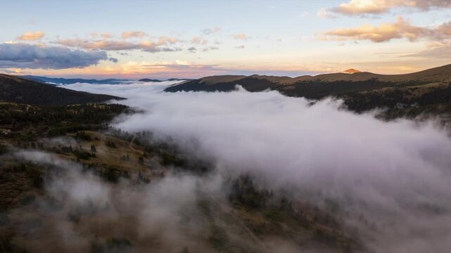 Backward rising drone hyperlapse over Waldorf ghost town near Georgetown, Colorado, as glowing sunset clouds frame rapidly evolving fog rolling up the mountain valley like ocean waves.