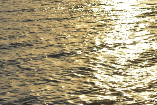 Close up view of sparkling golden sun glints and bright light reflections dancing on the rippling surface of open water during a late afternoon sunset