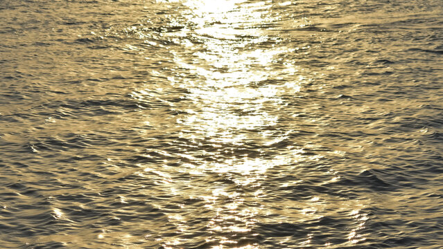 Close up view of sparkling golden sun glints and bright light reflections dancing on the rippling surface of open water during a late afternoon sunset