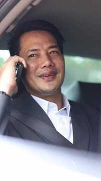 close up of Asian businessman in suit talking on smartphone inside car. Modern framing optimized for mobile display, social stories, business connection and mobile ads